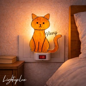 May include: Orange cat-shaped night light plugged into a wall outlet. The light has a black outline and the name "Vinny" in cursive. The light is on, illuminating the cat design. The brand name "LightupLux" is in the bottom left corner.