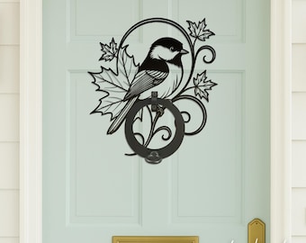 May include: Black metal door knocker featuring a bird perched on a ring, surrounded by maple leaves and decorative swirls. The bird has black and white markings. The door knocker is mounted on a light blue door.