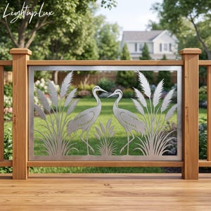 May include: A rectangular metal panel featuring a laser-cut design of two cranes standing among tall reeds. The silver-colored panel is framed by a wooden railing structure. The text Lightuplux is visible in the upper left corner of the image.
