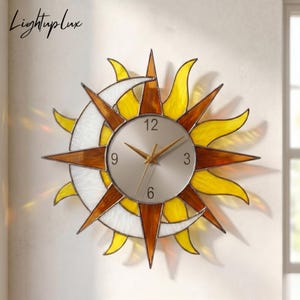 May include: A decorative wall clock featuring a sun and moon design. The clock has a silver face with gold hands and black numerals. The sun is made of yellow and brown glass, and the moon is white. The text "LightupLux" is in the upper left corner.