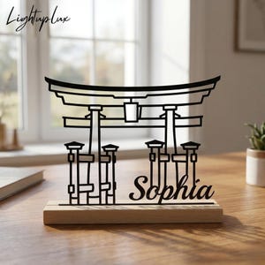 Könnte beinhalten: Eine schwarze Metall-Torii-Tor-Skulptur mit dem Namen "Sophia" auf einem Holzsockel. Die Skulptur ist ein dekorativer Gegenstand, möglicherweise für einen Schreibtisch oder ein Regal. Das Logo "LightupLux" befindet sich in der oberen linken Ecke.