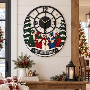 May include: A round black wall clock featuring a central dial with gold hands and numbers 3, 6, 9, and 12. Below the dial, five figures in winter clothing hold open books, flanked by two pine trees. The text THE SMITH FAMILY is printed at the bottom.