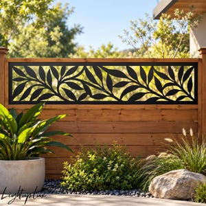 Peut inclure: Un panneau d'intimité rectangulaire en métal noir présentant un motif végétal découpé au laser. Le panneau est monté horizontalement dans un cadre de clôture en bois naturel, affichant un design organique de feuilles et de tiges.