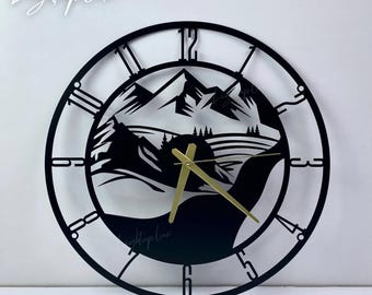 May include: A circular black wall clock featuring a cutout mountain landscape design with pine trees and a river. The clock face has open-frame numerals and gold-colored hour, minute, and second hands. The text LightupLux is visible in the top left corner.