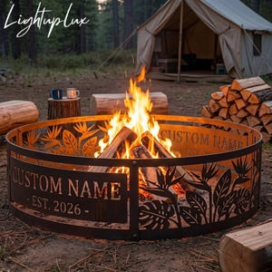 May include: A circular metal fire pit ring featuring laser-cut tropical leaf and bird of paradise flower patterns. The side panel displays the text CUSTOM NAME and EST. 2026. A bright orange and yellow fire burns inside the ring with logs.