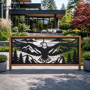 May include: A rectangular metal privacy screen featuring a laser-cut design of a soaring eagle with wings spread wide, set against a backdrop of jagged mountain peaks and evergreen trees. The black metal panel is framed by a natural wood border.