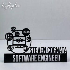 May include: Black metal desk sign for a software engineer. The sign features the name "STEVEN COGNATA" above the title "SOFTWARE ENGINEER". A computer screen graphic is surrounded by programming language symbols.