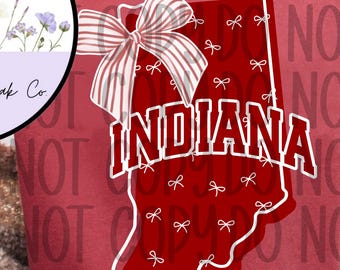 Może przedstawiać: Czerwony t-shirt z krótkim rękawem z grafiką stanu Indiana w kolorze czerwonym z białym obrysem. Kształt jest ozdobiony małymi białymi kokardkami i dużą kokardą w paski. Słowo INDIANA jest nadrukowane białymi literami na środku koszulki.
