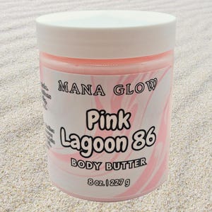 May include: A round, white-lidded jar of pink body butter. The label reads "MANA GLOW Pink Lagoon 86 BODY BUTTER" in black text over a pink and white swirl design. The jar contains 8 oz / 227 g of product.