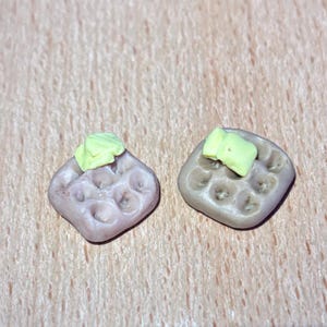 May include: Two miniature waffle-shaped pieces of clay with a yellow clay topping. The waffles are brown and the topping is a light yellow.