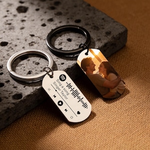 Könnte beinhalten: Zwei personalisierte Schlüsselanhänger. Einer zeigt ein Foto eines Paares, der andere ein Musikdesign mit dem Text "Sing a song Singer Taylor". Beide Schlüsselanhänger haben Metallringe.