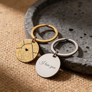 May include: Two keychains with round pendants. One gold-colored keychain features a map design with a heart, and the other silver-colored keychain has the text "I love you". Both keychains have metal rings.
