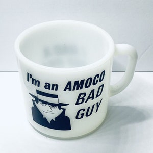 May include: White ceramic mug with a black and white illustration of a man in a hat and the text "I'm an AMOCO BAD GUY".
