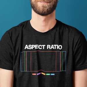 May include: Black t-shirt with the words "ASPECT RATIO" in white block letters. Below the text is a rectangular graphic with colored vertical lines and numbers. The shirt is worn by a person with a beard.