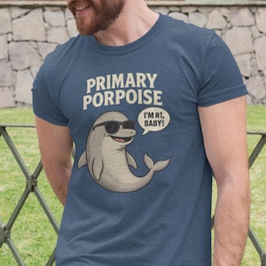 May include: Navy blue t-shirt featuring the text "PRIMARY PORPOISE" and a cartoon dolphin wearing sunglasses. The dolphin has a speech bubble that says "I'M #1, BABY!"