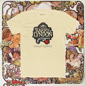 May include: A cream-coloured t-shirt with the film title "Barry Lyndon" in black and white, a pistol, and a red rose. The text "Stanley Kubrick" is below. The shirt is set against a vintage-style background with illustrations.