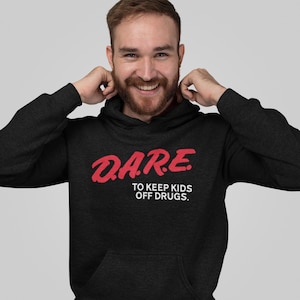 May include: A charcoal grey hooded sweatshirt featuring the red text D.A.R.E. and the white text TO KEEP KIDS OFF DRUGS. The garment includes a front kangaroo pocket, long sleeves, and a hood with matching drawstrings in a heathered fabric finish.