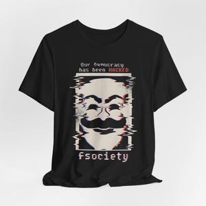 Op de afbeelding: Zwart T-shirt met een gestileerde afbeelding van een Guy Fawkes-masker met een glitch-effect. De tekst "Our democracy has been HACKED" staat boven het masker, en "fsociety" eronder.
