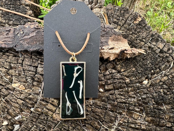 Actual rodent bones suspended in UV resin and set in a gold steel pendant — wearable oddity jewelry that's genuinely weird in the best way.