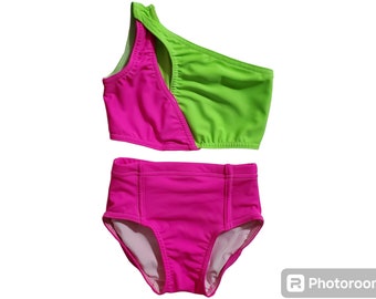 May include: A two-piece swimsuit with a bright pink bottom and a green and pink top. The top is one-shouldered and has a cut-out detail.