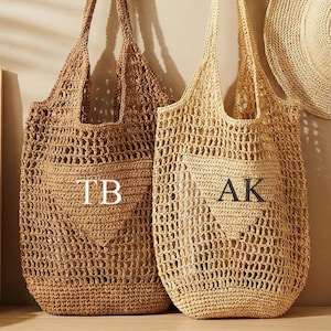 Può includere: Due borse tote intrecciate, una marrone e una beige, ciascuna con un'iniziale. Un cappello di paglia è appeso a un attaccapanni di legno sopra le borse. Una stampa incorniciata e una bottiglia di birra sono visibili.