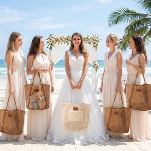 Pode incluir: Uma noiva e damas de honra numa praia, cada uma segurando uma sacola de tecido. As sacolas s&atilde;o de cor castanho natural com formato retangular e um patch de couro. As mulheres usam vestidos longos e esvoa&ccedil;antes de cor clara. Um arco de casamento est&aacute; ao fundo.