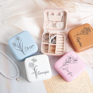 May include: Several small, square jewellery boxes in pastel shades of blue, white, pink, and tan. Each box has a floral design and a name. One is open, showing compartments for rings and necklaces.