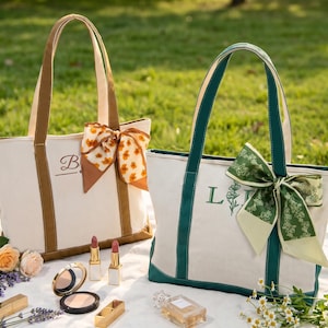 Peut inclure: Deux sacs fourre-tout en toile, l'un avec une bordure marron et un foulard floral, l'autre avec une bordure vert foncé et un foulard à motifs verts. Les deux sacs présentent des lettres brodées sur le devant et des produits cosmétiques.