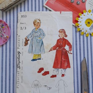 May include: A vintage sewing pattern for children's robes. The pattern is for sizes 2 and 3 and is from Pictorial Simplicity. The pattern features two children wearing robes, one in blue and white stripes and the other in red. The pattern is on a white background with black text.