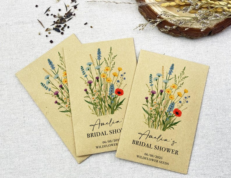 Op de afbeelding: Drie kraftpapieren enveloppen met zakjes met wilde bloemenzaad. Elke envelop heeft een bloemenontwerp en de tekst "Amelia's Bridal Shower" met de datum "06/08/2023" en de woorden "Wildflower Seeds".