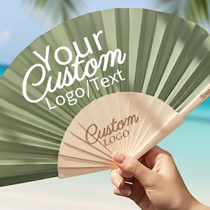 May include: A green and beige folding fan with the text "Your Custom Logo/Text" and "Custom Logo" printed on the fan. The handle reads "Your Custom Text". The fan is held in front of a blurred tropical background.