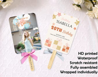 May include: Two personalized birthday fans. One features a photo with balloons and the text "Welcome to My Birthday". The other fan says "Birthday Isabella 20th Birthday" with event details. Both have wooden handles and decorative bows.