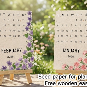 Könnte beinhalten: Zwei kleine Holzstaffeleien zeigen Saatpapierkalender für Januar und Februar 2026. Der Januar-Kalender zeigt rosa Rosen, während der Februar-Kalender lila Blumen hat. Der Text "Seed paper for planting" und "Free wooden easel" befindet sich unten.
