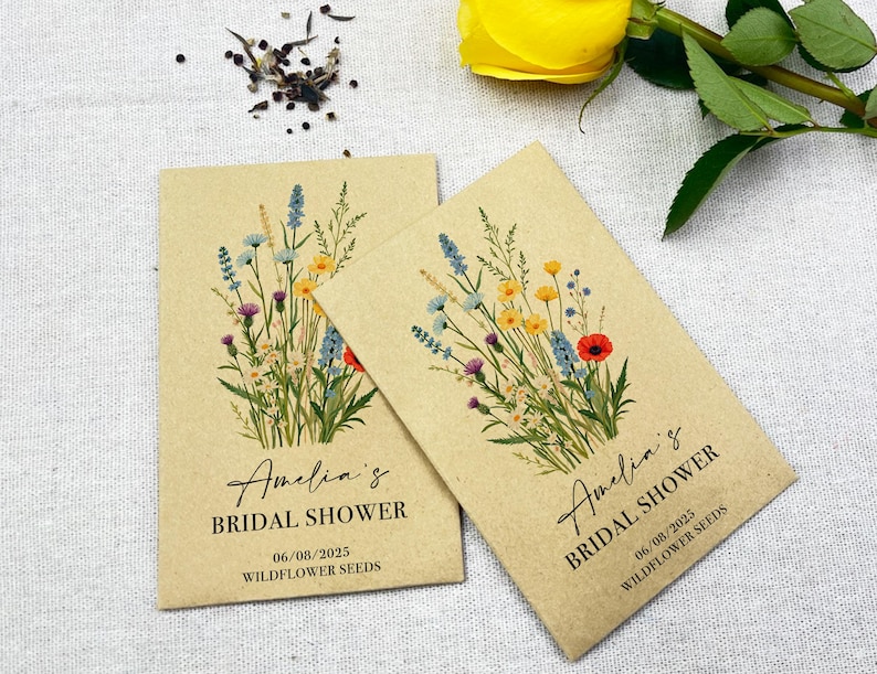 Op de afbeelding: Twee kraftpapieren enveloppen met zakjes wilde bloemenzaad. De enveloppen hebben een bloemenontwerp met verschillende kleuren, waaronder blauw, geel, rood en groen. De tekst op de enveloppen luidt "Amelia's Bridal Shower" en "06/08/2025 Wildflower Seeds".