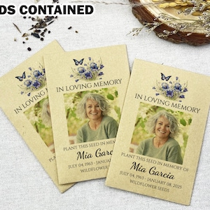 May include: Three beige seed packets with the text "IN LOVING MEMORY" and a photo of a woman. Each packet has a floral design with a butterfly. The text "PLANT THIS SEED IN MEMORY OF Mia Garcia" is also visible. The words "SEEDS CONTAINED" are at the top.