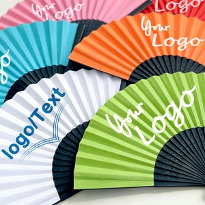 Op de afbeelding: Een verzameling kleurrijke papieren waaiers met zwarte handvatten. De waaiers zijn in verschillende kleuren, waaronder roze, blauw, oranje, wit en groen. Elke waaier heeft de tekst "Your Logo" of "logo/Text" in wit of blauw.