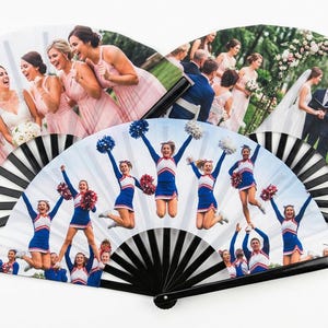 Op de afbeelding: Drie opvouwbare handwaaiers met zwarte kunststof ribben, elk met een andere fotoprint. Eén waaier toont een bruiloftsgroep in roze jurken, een andere een huwelijksceremonie onder een bloemenboog en de derde toont springende cheerleaders.