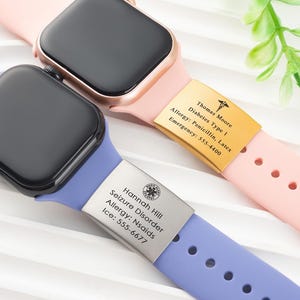 Puede incluir: Dos smartwatches con pantallas negras y correas coloridas. Uno tiene una correa rosa con una etiqueta de identificación médica dorada, y el otro tiene una correa azul con una etiqueta de identificación médica plateada. Las etiquetas muestran información médica.