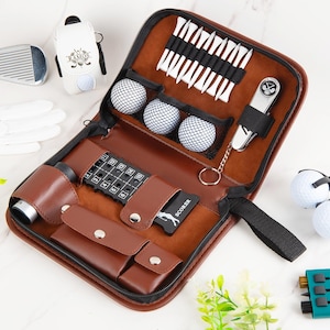 May include: A brown leather golf kit with a zipper, containing golf balls, tees, a scorecard, and a rangefinder. Additional items include a golf club, glove, and a golf ball holder. The kit is designed for golfers.