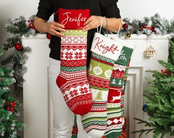 May include: Three Christmas stockings with personalized names. The stockings are red, white, and green with snowflake, tree, and reindeer patterns. Each stocking has a white cuff with a name in red script.