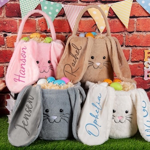 Könnte beinhalten: Fünf Plüsch-Osterhasen-Körbe in Rosa, Beige, Grau und Weiß, jeweils mit einem Hasengesicht und langen Ohren. Die Körbe sind mit dekorativen Ostereiern und Stroh gefüllt. Namen sind auf die Ohren gestickt.