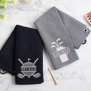 May include: Two personalized golf towels, one gray and one black, with embroidered golf-themed designs and names "Lauren" and "Becker".