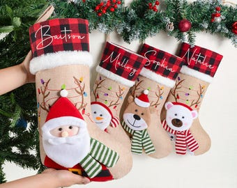 May include: Christmas stockings with personalized names in script on red and black plaid cuffs. The stockings are beige with festive designs, including a Santa, snowman, reindeer, and polar bear.