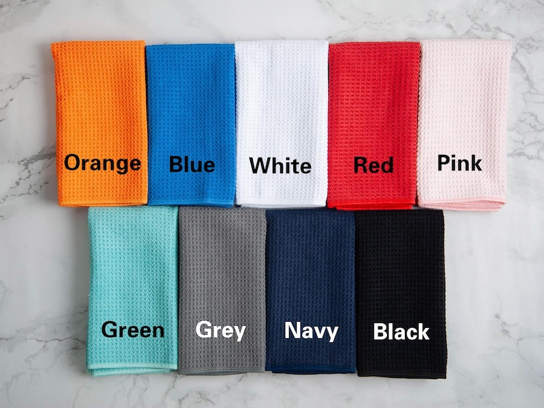 May include: Ten waffle weave kitchen towels in different colors: orange, blue, white, red, pink, green, grey, navy, and black. Each towel has the color name printed on it.