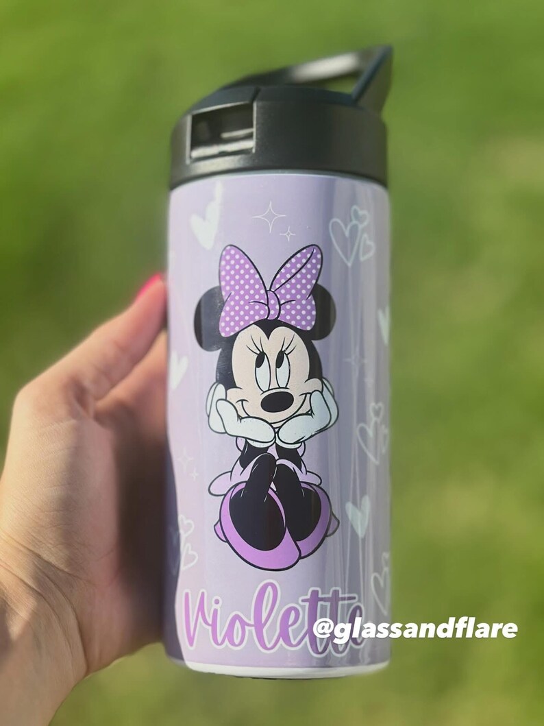 Puede incluir: Una botella de agua morada con Minnie Mouse, un lazo de lunares y el nombre "Violetta". La botella tiene una tapa negra y corazones blancos. Tambi&eacute;n se ve el texto "@glassandflare".