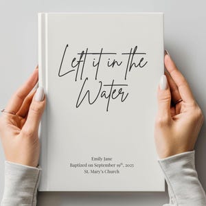 May include: A white book with the words "Left it in the Water" in black script. The book also includes the name "Emily Jane", the date "September 19th, 2025", and "St. Mary's Church".