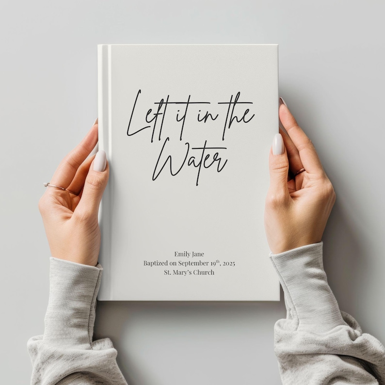 May include: A white book with the words "Left it in the Water" in black script. The book also includes the name "Emily Jane", the date "September 19th, 2025", and "St. Mary's Church".