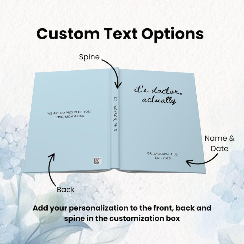 May include: Light blue notebook open to reveal the text "it's doctor, actually" on the right page. The left page reads "WE ARE SO PROUD OF YOU! LOVE, MOM & DAD". The spine reads "DR. JACKSON, Ph.D". The bottom of the right page reads "DR. JACKSON, Ph.D EST. 2026".