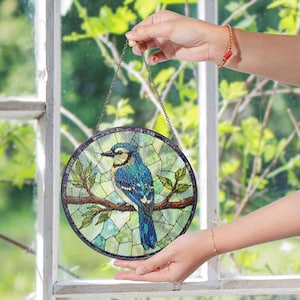 a hand holding a stained glass bird hanging from a window