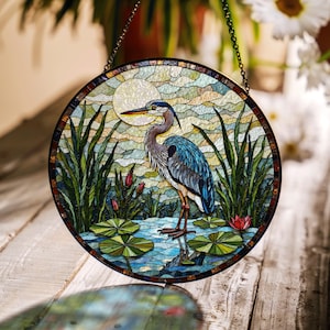 May include: Round stained glass panel featuring a blue heron standing in a pond with lily pads. The artwork includes a full moon, reeds, and a colorful mosaic background. A decorative piece with a chain for hanging.